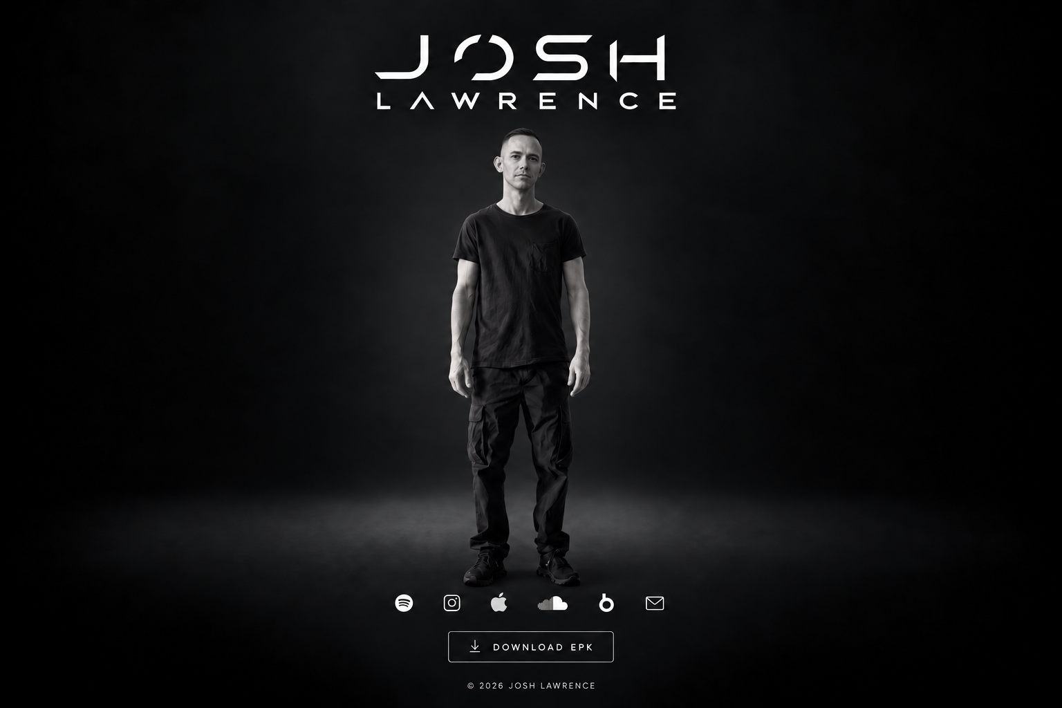 Josh Lawrence in a black T-shirt and trousers, standing against a dark studio backdrop